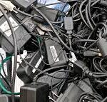 A tangled collection of old laptop chargers, AC power adapters, and black electronic cable scrap gathered for e-waste recycling.
