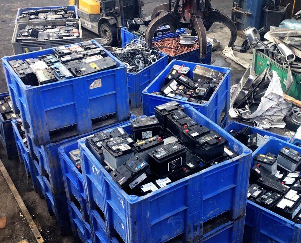 Stacks of blue industrial crates filled with used car batteries at a scrap recycling facility